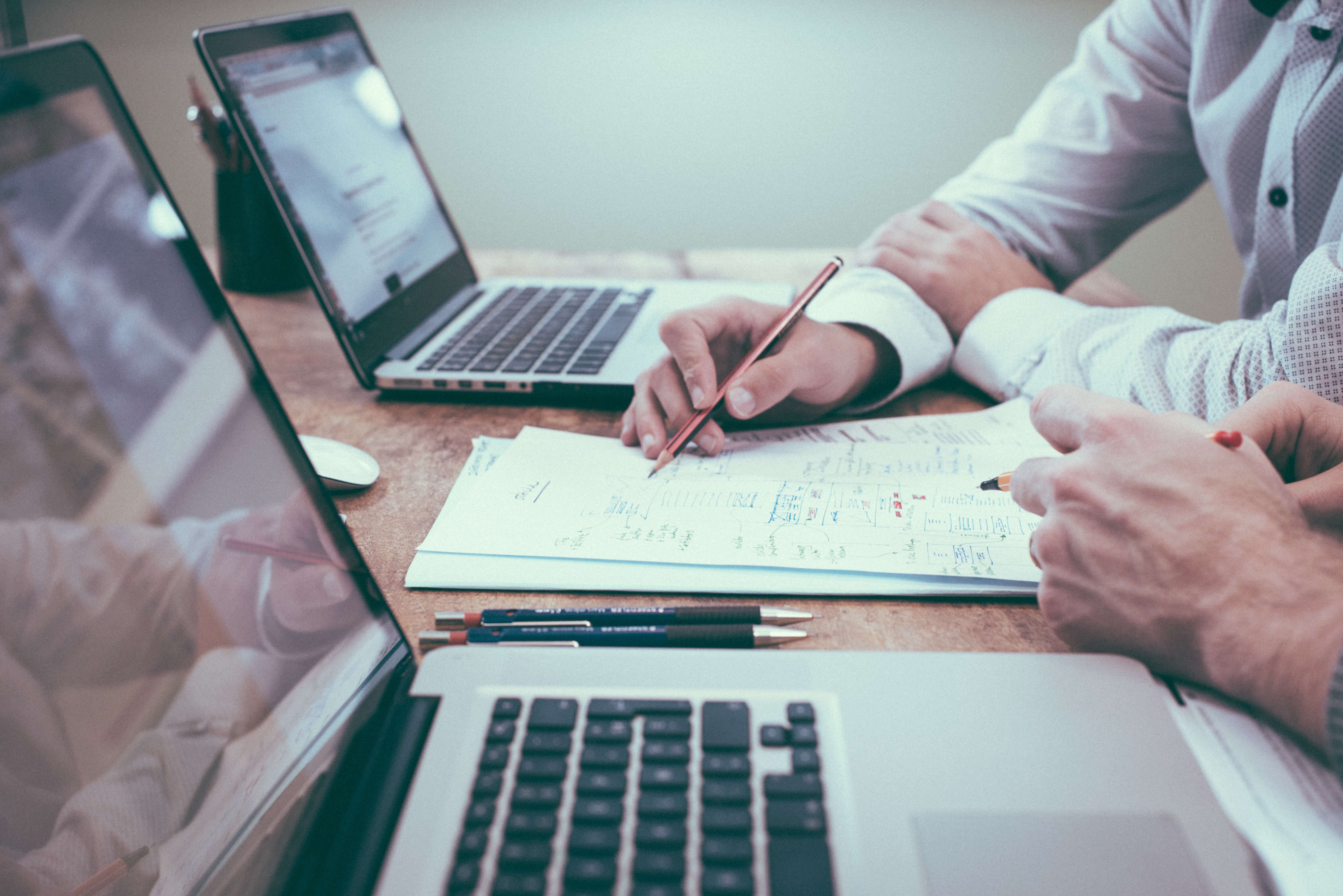 two people working together on paperwork with laptops