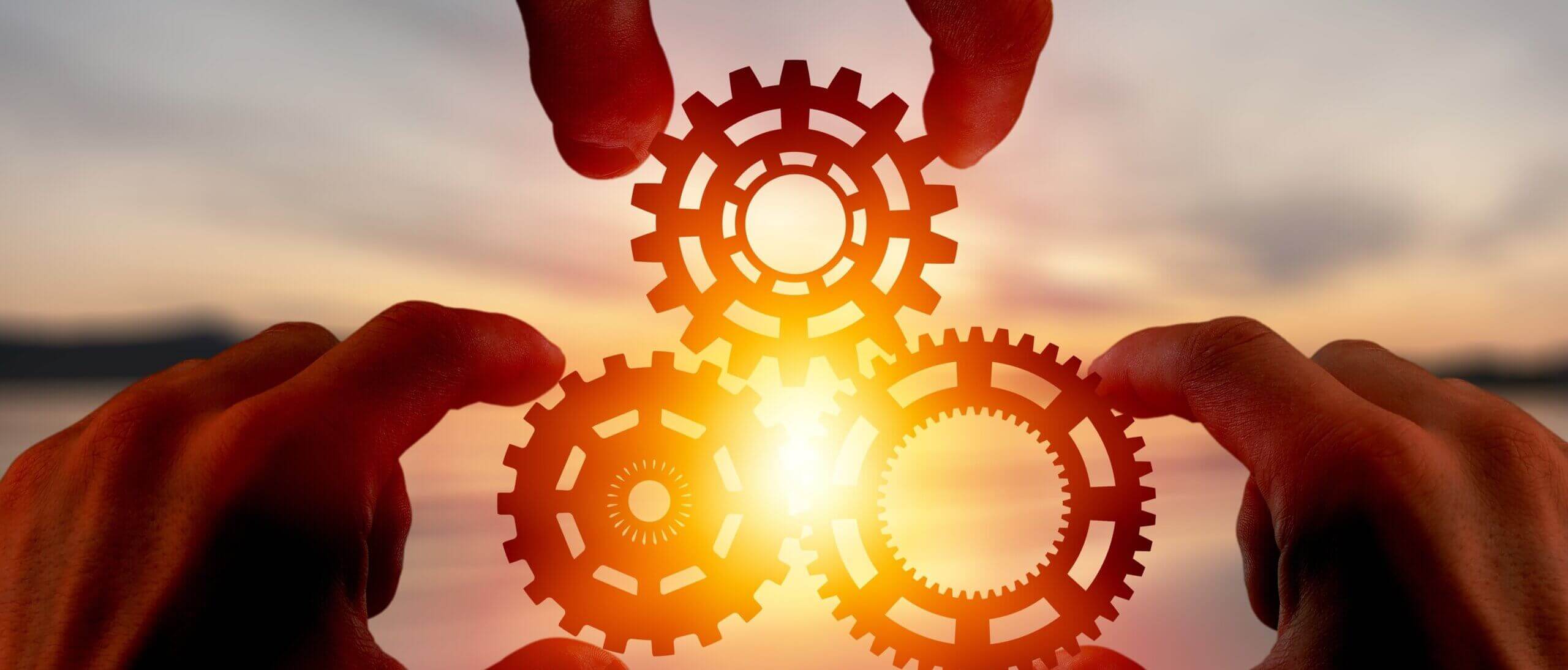 hands holding gears with sunset